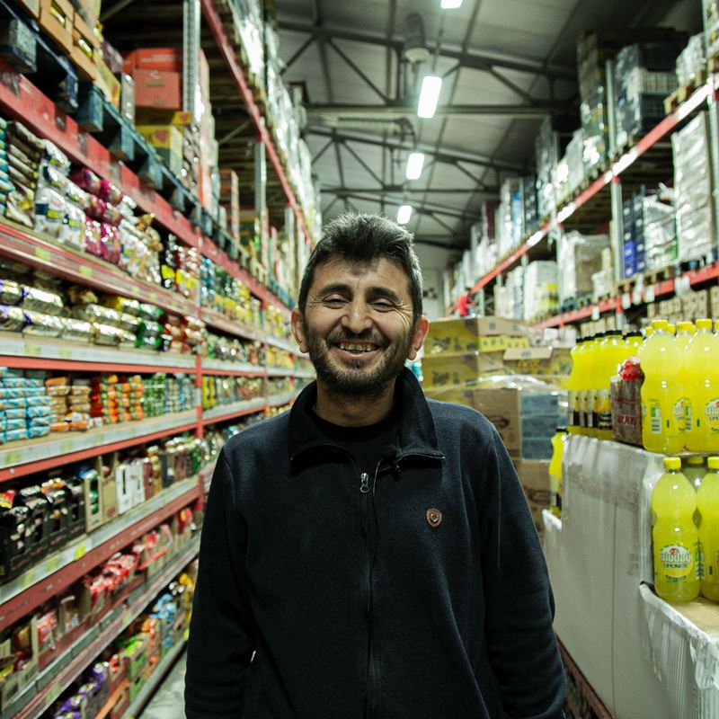 Gultekin, a store owner, feels happy in his store in Kahramanmraş after his sales improved thanks to DRC's Cash and Voucher Assistance (CVA) response in March 2023. CVA response partnered with local stores to ensure access to essential goods to those in need. 